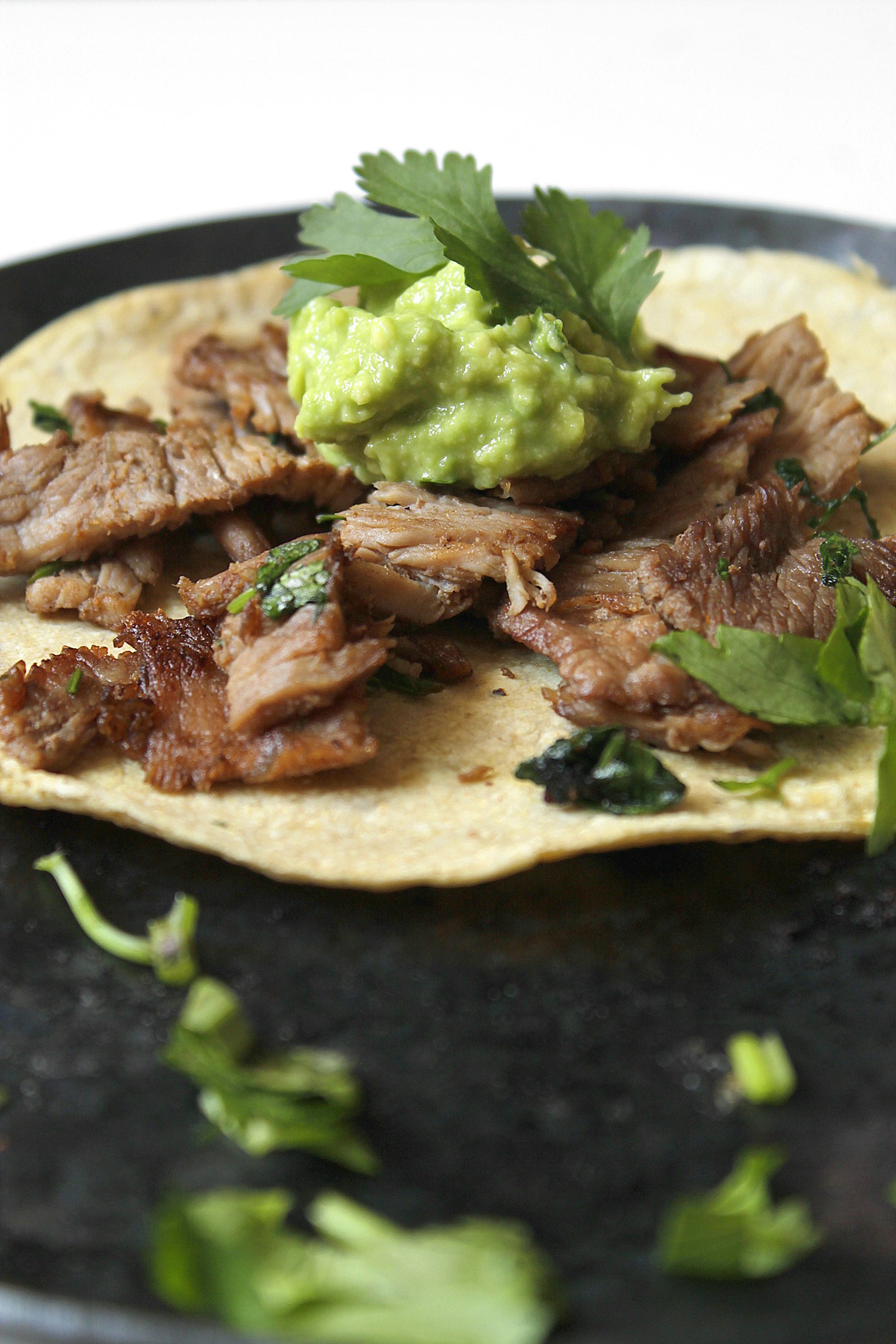 Carne asada sobre tortilla de maíz en un comal oscuro, imagen representativa